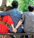 a man sitting with arms over a woman who secretly is having an affair holding hands with her lover
