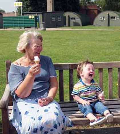 Grandmother sitting along with grandchild on a bench eating ice-cream and having fun