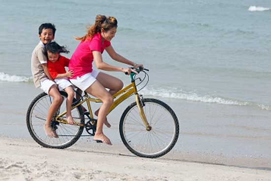 Mother riding bicycle with kids at the back on a beach during vacations