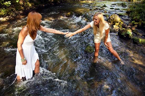 one girl helping other girl to cross stream