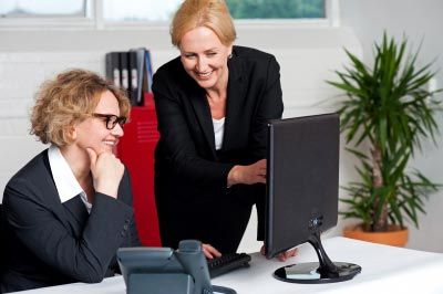 A woman helping other woman on computer in office