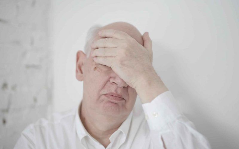 An elderly man in depression covering his head by hand