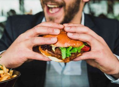 Man eating burger with hands to satisfy hunger or appetite