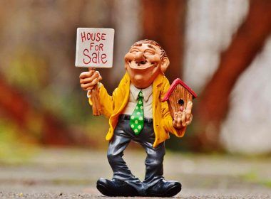 An animated man with house model and placard in hand trying to sell his house