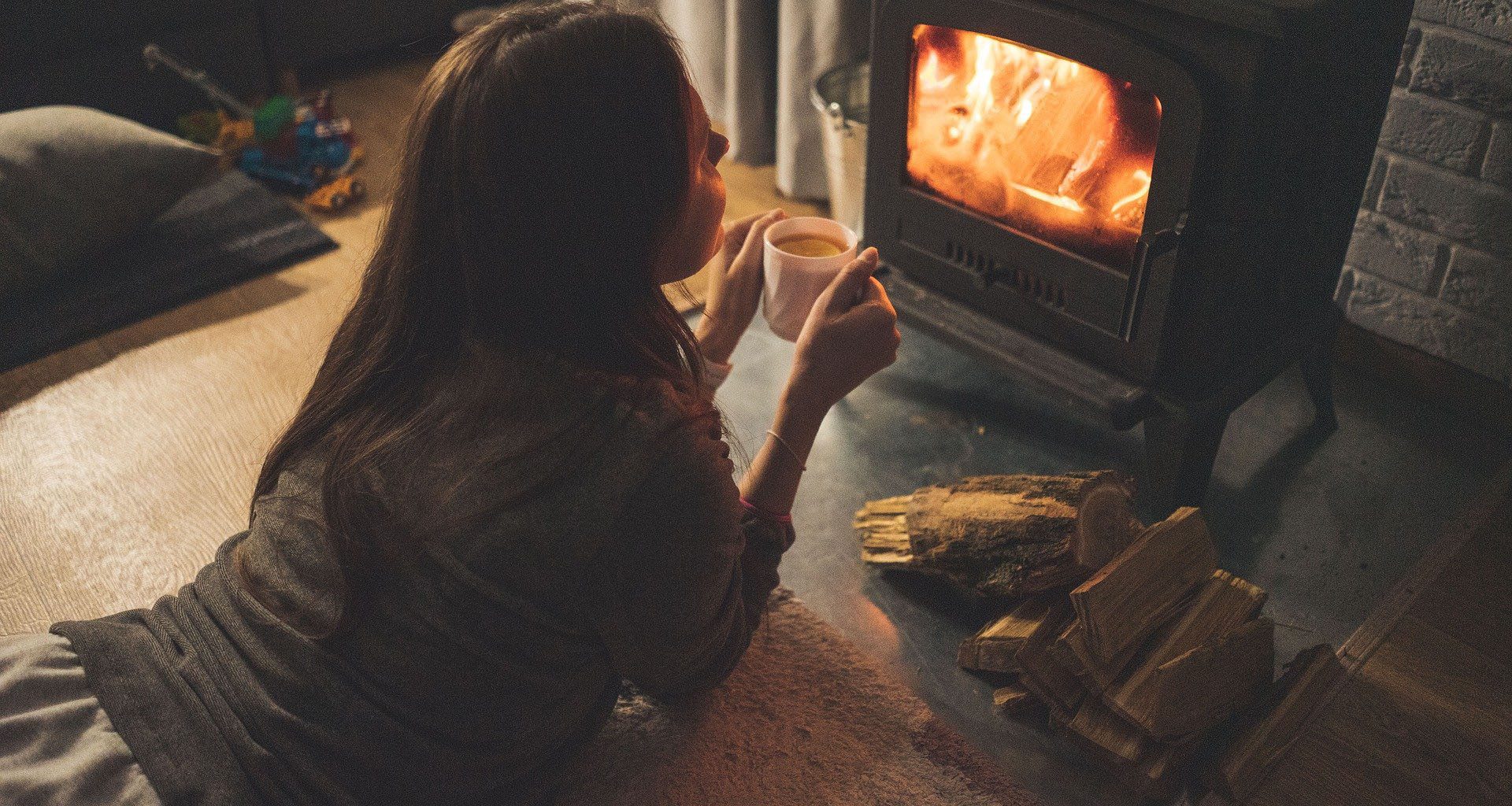 A girl enjoying coffee lying down in front of a woodfire heater in winter