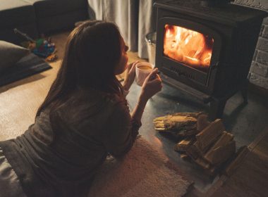 A girl enjoying coffee lying down in front of a woodfire heater in winter