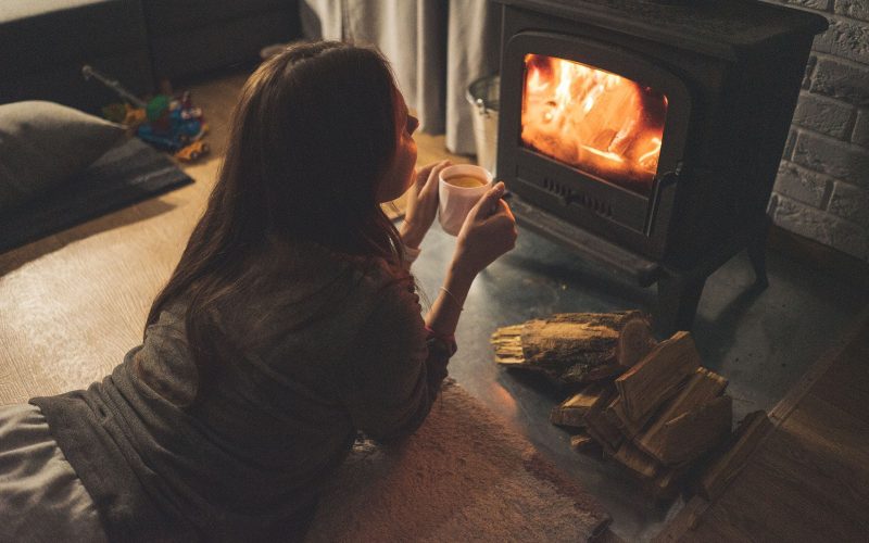 A girl enjoying coffee lying down in front of a woodfire heater in winter