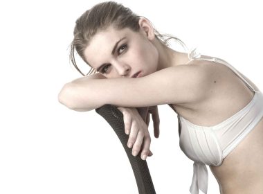 A white woman wearing white bra lingerie sitting on a chair