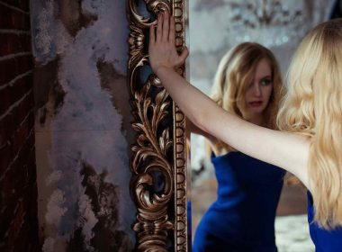 A blonde narcissist woman standing and viewing herself in a mirror