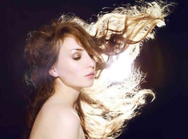 Wind blowing the healthy hair of a woman against a dark background.