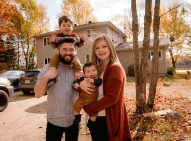 A happy family of parents and children standing in front of their safeguarded house.