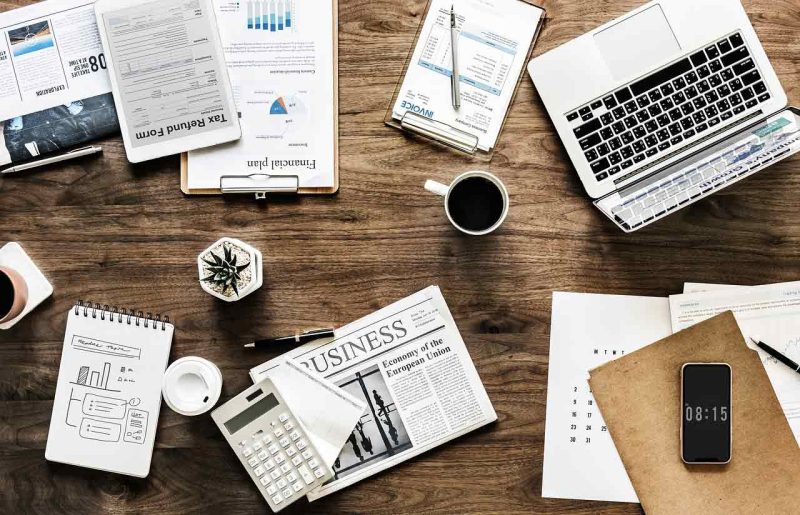 A laptop, coffee cup, and business expansion plan papers on a table.