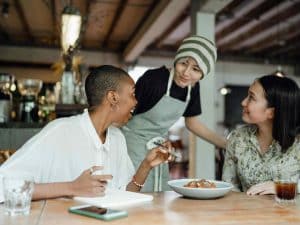 Happy customers at a table in a restaurant attended by a waiter